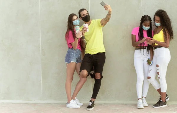 Young people group with face mask waiting to get in the supermarket.  Multiracial people making selfies and looking videos. Coronavirus and spread virus prevention concept. Image