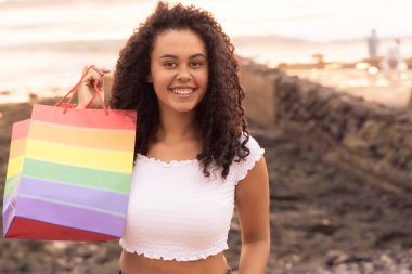 Genç kız bir gökkuşağı çantası tut. Cinsel azınlık ve LGBT kavramı. Kumsalda alışveriş yaptıktan sonra mutlu bir kadın. LGBT ve tatil konsepti.