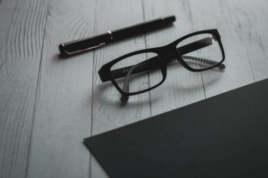 Bir gözlük ve siyah arka planda bir kalem. İş konsepti. Metin için kara liste