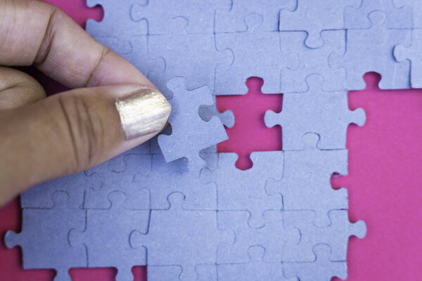 Female hand fitting a puzzle piece on pink background Conceptual of love, connection, romanticism
