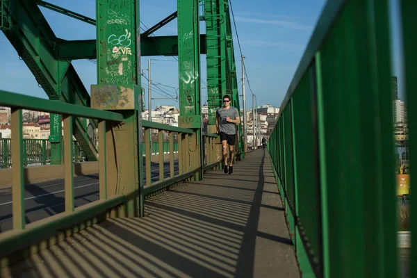 Active healthy man jogging by green bridge at daytime