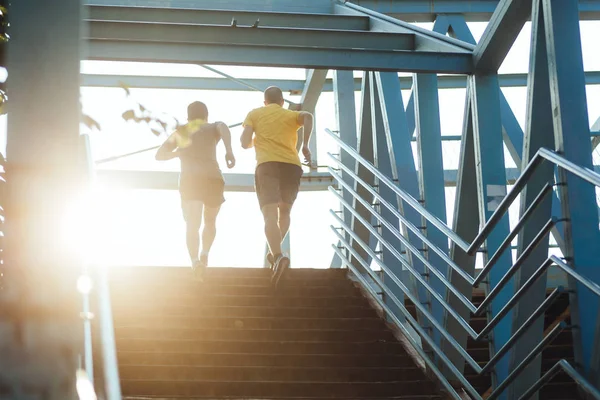 Two professional male athletes running on the bridge