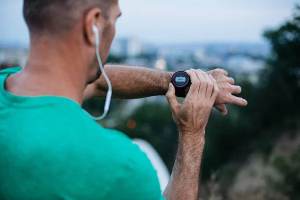 Close view of professional male athlete preparing headphones and smartwatch before jogging