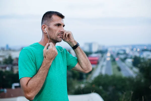 Professional male athlete preparing headphones and smartwatch before jogging