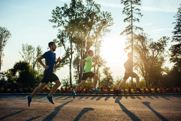 Three professional male athletes running in park at sunset