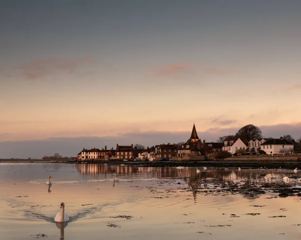 sunrise reflections at bosham quay in west sussex with swans swimming on the rising tide