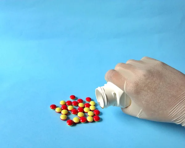 Mão com luva branca esvaziando um pillbox de pílulas amarelas e vermelhas. conceito médico — Fotografia de Stock