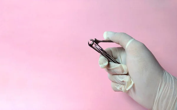 Mano con guanto bianco con un tagliaunghie per la cura di un paziente su sfondo rosa. concetto medico — Foto Stock