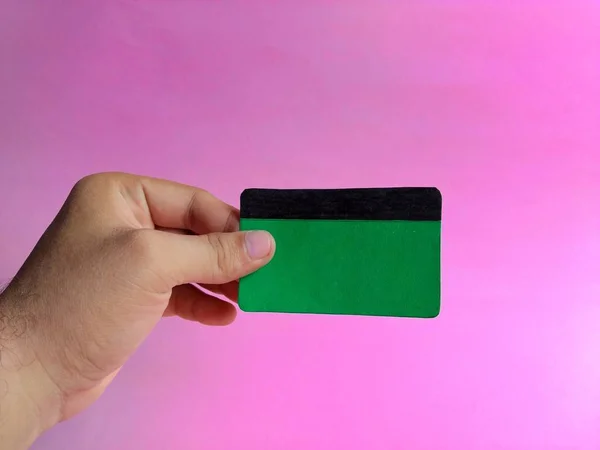 Pembe arka planda boş yeşil bir kredi kartı tutuyor. finans kavramı