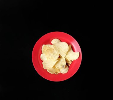 Siyah arka planda kırmızı tabakta patates cipsi. abur cubur kavramı
