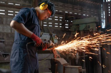 Fabrika atölyesinde endüstriyel elektrikli aletler kullanan çeşitli Asyalı makine mühendisi sıcak metal kıvılcımlarına neden oluyor.