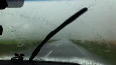 Şiddetli yağmurda çalışan cam silecekleriyle arabanın ön camının görüntüsü. Sağanak yağış sırasında arabanın içinden fırtına bulutlarını izle. Yağmurlu bir günde silecekleri çalıştır.