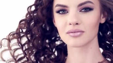 Uzun kıvırcık saçlı güzel bir kadın. Güzel surat. Moda modeli. Moda makyajı. Göz makyajlı çekici bir kız. Bir kızın yakın çekim yüzü. Yavaş çekim 4K görüntüsü. Seksi esmer bayan..  