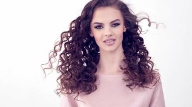 Uzun kıvırcık saçlı, gülümseyen güzel bir kadın. Güzel surat. Moda modeli. Moda makyajı. Göz makyajlı çekici seksi bir kız. Bir kadının yakın çekim yüzü. Yavaş çekim 4k görüntü.   