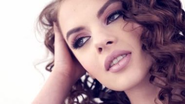 Uzun kıvırcık saçlı güzel bir kadın. Güzel surat. Moda modeli. Moda makyajı. Göz makyajlı çekici bir kız. Bir kızın yakın çekim yüzü. Yavaş çekim 4K görüntüsü. Seksi esmer bayan..  