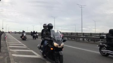 Şehirde büyük bir motosiklet konvoyu geziyor. Modern motosikletli motorcular şehir otoyolu boyunca ilerliyorlar. Büyük bir motosiklet sürücüsü grubu yolda ilerliyor. Koşan motosikletlerin gürültülü sesleri. 