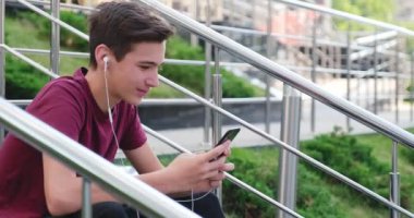 Parkta cep telefonu kullanan bir genç. Açık havada cep telefonu kullanan gülümseyen genç bir adam. Cep telefonu olan mutlu bir çocuk. Şehir manzarası. Yakışıklı adam akıllı telefon kullanıyor. 4 bin. Gerçek zamanlı..