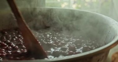 Kiraz reçeli pişiriyorum. Reçel pişirme. Mutfak spatulasıyla leğen kemiğinde kiraz reçeli pişiriyorum. Adam kiraz reçelini karıştırıyor. Ağır çekim. 4k görüntü. 