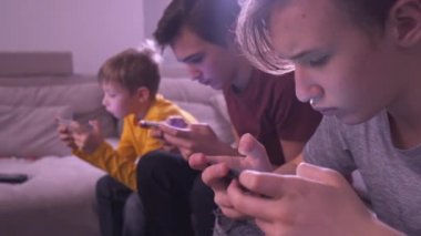 Evde akıllı telefonları olan çocuklar. Üç çocuk cep telefonu kullanarak sosyal ağda vakit geçiriyor. Beyaz çocuklar oyun için cep telefonu kullanıyor. Yaşam tarzı konsepti. Tam zamanlı gerçek zamanlı görüntüler.  
