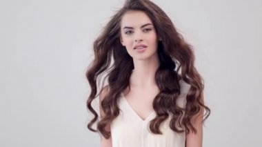 Uzun kıvırcık kahverengi saçlı güzel bir kadın. Moda modeli stüdyodaki kameraya bakıyor. Çekici esmer bir kadının yakın çekim yüzü. Saexy görünüşlü seksi bir manken. 4K görüntü. Yavaş çekim. 