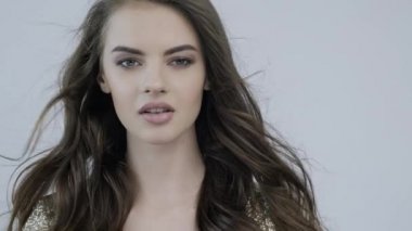 Kıvırcık uzun kahverengi saçlı güzel bir kadının 4K görüntüsü. Moda modeli kameraya bakıyor. Kafkasyalı bir kızın çarpıcı yüzü. Güzel gözleri olan seksi bir manken. Ağır çekim. Güzellik konsepti 