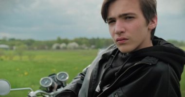 Genç adam bir motosiklete biner ve yazın doğadaki mesafeye bakar. Sakin durumdaki bir genç yaz günü doğayı düşünür. Erkek motosikletçi uzaklara baktı.