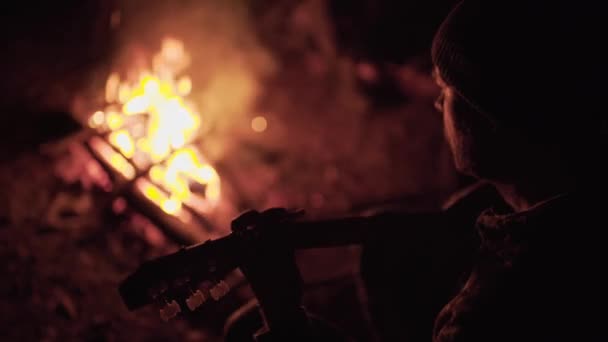 人类在大自然的篝火边弹奏吉他 在大自然的火边度周末 成年人晚上在火堆边的森林里歇息 — 图库视频影像