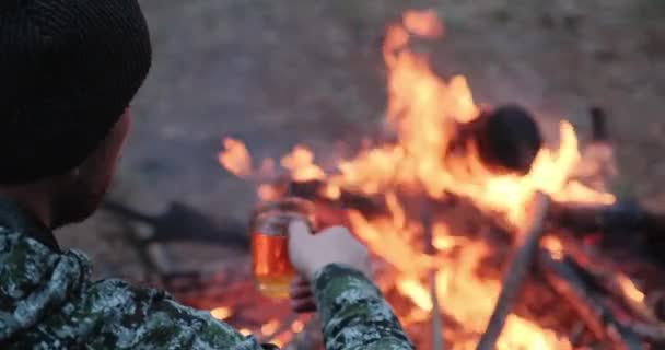 人在森林的火边喝热茶 人类看着火 喝着关于大自然的茶 一个人坐着 在火边休息 晚上喝一杯咖啡 这是他的后视镜 — 图库视频影像