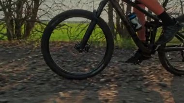 Erkek ayağının yavaş hareketi bir dağ bisikletinin pedallarını çevirir. Çakıl taşları üzerinde bisiklet tekerleğinin yakın çekimi. Bisiklet tekerleği hareket halindeyken çekilen çekim. Bisikletçi bisikletle pedal çeviriyor. Bisiklet lastiği 