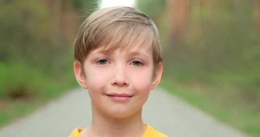 Doğaya bakan küçük bir çocuğun yakın çekim yüzü. 8 yaşındaki beyaz çocuk dışarıda dikiliyor. Yavaşça çocuğun yüzüne doğru yakınlaştırıyorum. Sevimli okullu sarışın, mavi gözlü, gülümseyen bir çocuk.