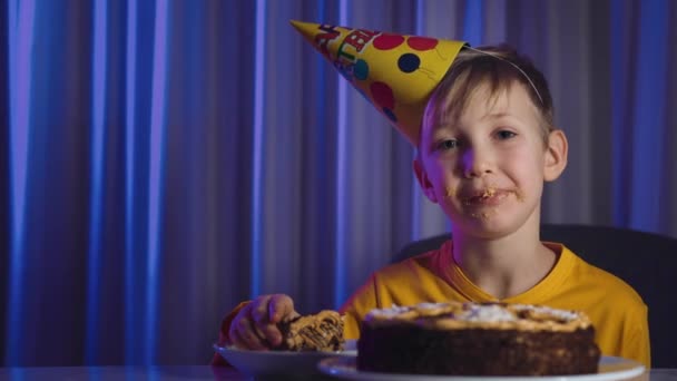 幸せな子供はお祝いのケーキの部分を取り それをかむと飲み込む かわいい男の子は誕生日にケーキを食べる 頭にコーンと幸せな少年は彼の誕生日を祝う 白人の子供と誕生日ケーキ — ストック動画
