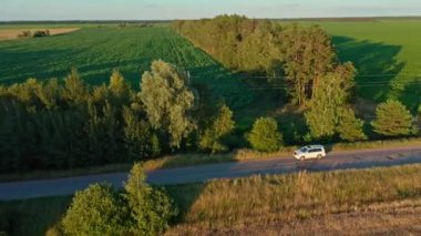 Hava aracı görüntüsü: beyaz SUV aracı yola çıkıyor. Drone, yolda giden bir arabayı takip ediyor. Araba macerası işte. Hareket halindeki arabaya üstten bak. 