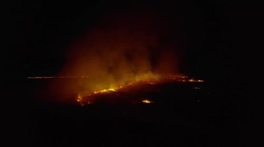 Gece vakti ateş yakarak sahada uçmak. Dramatik video çekimi, duman bulutları, ateşin yayılması. İklim değişikliği, ekoloji. Kontrolsüz kırsal yangın. Kuru otların yanması