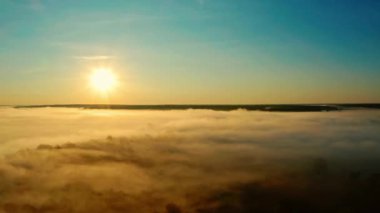 Manzaralı hava manzarası: Güneş doğarken hareket eden altın bulutlar, ağaçların üzerinde mavi gökyüzü. Drone, akşam vakti parlak güneşin altında mavi gökyüzünde kabarık bulutların arasından ileri doğru uçar. Gün batımında bulutlu güneş  