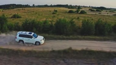 Yavaş bir hareket yap. AERİAL VİEW. Beyaz SUV arabası kırsal yolda hızla gidiyor. İnsansız hava aracı büyük toz bulutlarıyla ülkeyi boydan boya geçen bir arabayı takip ediyor. Arkasında toz bulutu bırakan hızlı araba. 