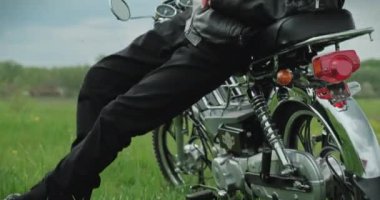 Genç adam bir motosiklete biner ve yazın doğadaki mesafeye bakar. Sakin durumdaki bir genç yaz günü doğayı düşünür. Erkek motosikletçi uzaklara baktı.