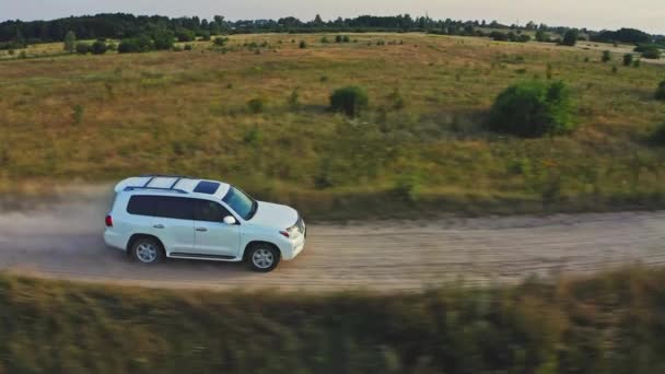 电影空中景观 白色越野车在夏日落山时驾驶 无人机正跟随一辆汽车在一个黄色的田野上穿越国境 在大自然中乘坐汽车旅行 — 图库视频影像