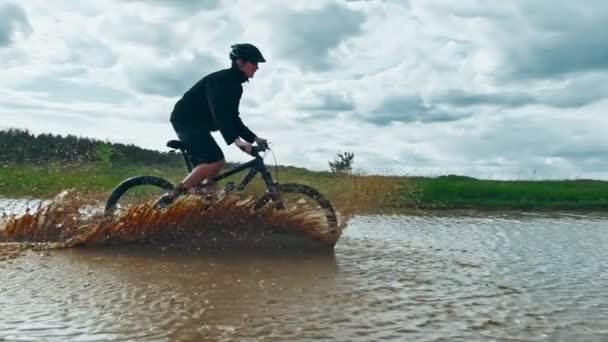 남자가 자전거를 커다란 웅덩이로 들어갑니다 사이클 러스는 더러운 물보라를 만들어 — 비디오