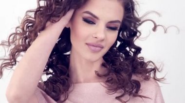 Uzun kıvırcık saçlı, gülümseyen güzel bir kadın. Güzel surat. Moda modeli. Moda makyajı. Göz makyajlı çekici seksi bir kız. Bir kadının yakın çekim yüzü. Yavaş çekim 4k görüntü.   