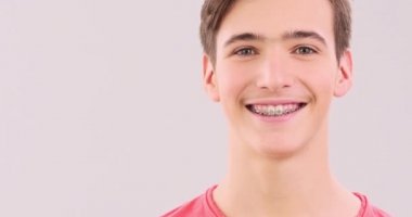 Dişlerinde diş telleri olan gülümseyen genç bir adam. Yakışıklı, sağlıklı dişleri olan, kameraya bakan, yakından gören bir çocuk. Gerçek zamanlı çekim 50 fps ProRes. Gülümseyen insan yüzü.