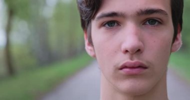 Genç üzgün adam kameraya bakıyor. Mutsuz, yalnız, genç bir delikanlı, açık havada. Hüzünlü bakışları olan yakışıklı bir adamın yakın çekim yüzü. Hüsrana uğramış genç yüzü, dışarıda.