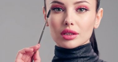Kadın makyaj yapıyor. Genç bir kadın kirpiklerini kirpik fırçasıyla boyuyor. Kozmetik konsepti. Güzel esmer model makyaj yapıyor. 4K Ağır çekim. Yakın görünüm.