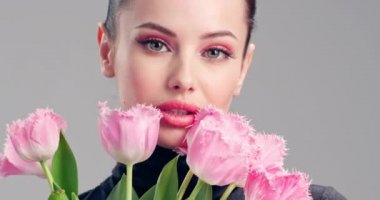 Çiçekli güzel beyaz kız. Pembe lalelerden oluşan büyük buket çiçekleriyle göz kamaştırıcı esmer kız. Temiz ciltli, genç ve güzel bir kadının yakından çekilmiş yüzü. Parlak makyajlı kadın. 