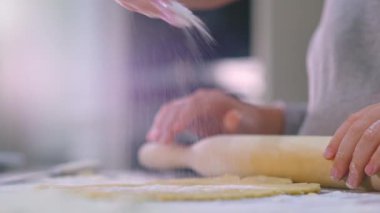Yavaş çekim 4K görüntü - anne ve çocuğun elleri merdaneyle hamuru yuvarlıyor, makro. Annesi olan çocuk hamuru mutfak masasına koyuyor. Evde aile yemekleri.. 