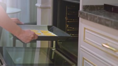 Kadın fırına kurabiye dolu bir çarşaf koyuyor. Kadınların elleri fırına kurabiye dolu bir yemek tepsisi taşır. Ev hanımı şekerli kurabiye pişiriyor. Kupa şeklinde kurabiyeler. Yavaş çekim görüntüleri