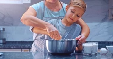 Yavaş çekim 4K, anne ve çocuk çelik kasede hamur karıştırıyor. Annesi mutfakta yemek yapan bir çocuk. Evde aile yemeği pişirmek. Anne ve oğlu kurabiye pişirmek için malzemeleri karıştırıyor. 