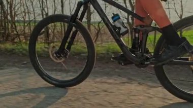 Bisiklet pedallarını pedallara çeviren bisikletçinin yavaş hareketi. Çakıl taşları üzerinde bisiklet tekerleğinin yakın çekimi. Bisiklet tekerleği hareket halindeyken çekilen çekim. Erkek ayağı bir dağ bisikletinin pedallarını çevirir. Bisiklet lastiği 