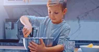 Yavaş çekim 4K, çocuk mutfakta yemek pişiriyor. Beyaz çocuk kurabiye için hamur karıştırıyor. Çocuk, çelik kasede kek malzemelerini karıştırıyor. 8 yaşındaki çocuk evde yemek pişiriyor.. 