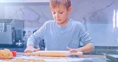 Merdaneli hamuru yuvarlayan çocuk, yakın görüş. Çocuk hamuru mutfak masasının üzerine atıyor. 8 yaşındaki çocuk evde yemek hazırlıyor. Çocuk merdaneyle hamuru yuvarlıyor. Yavaş çekim 4k görüntü 