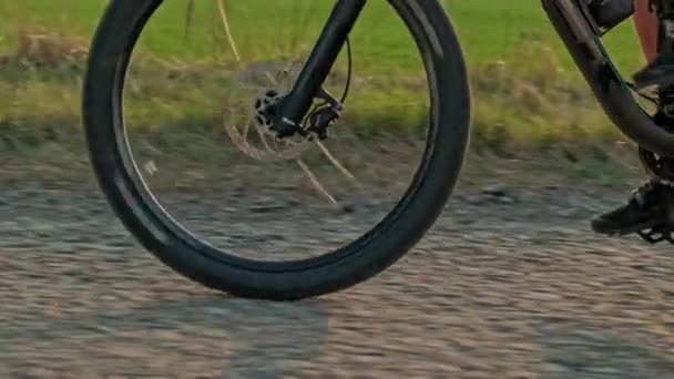 Zpomalený pohyb pánských nohou otáčí pedály horského kola. Detailní záběr kola, které jede na štěrku. Sledování pohybu kola. Cyklista šlape pedály na kole. Kolo 